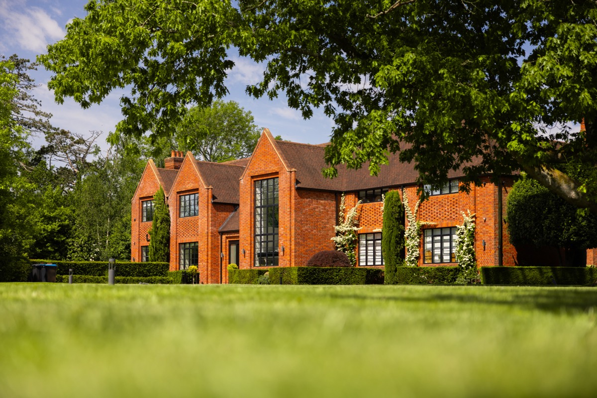 A red brick country house framed by a mature tree across a lawn