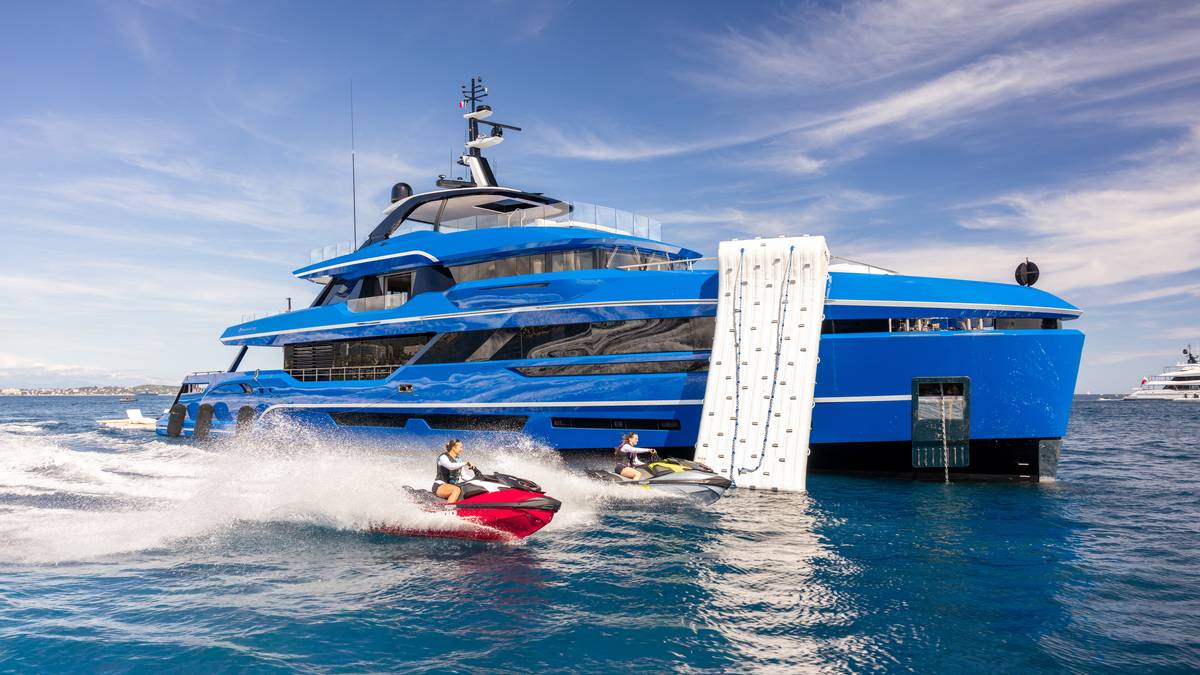 A blue-hulled superyacht under way with jet skis alongside