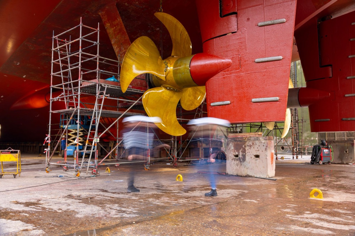 A ship&rsquo;s propeller in dry dock, with technicians moving past it