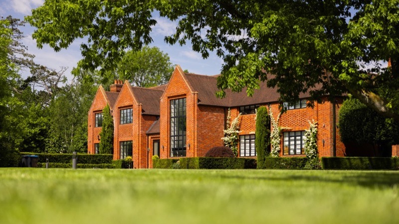 A red brick country house framed by a mature tree across a lawn