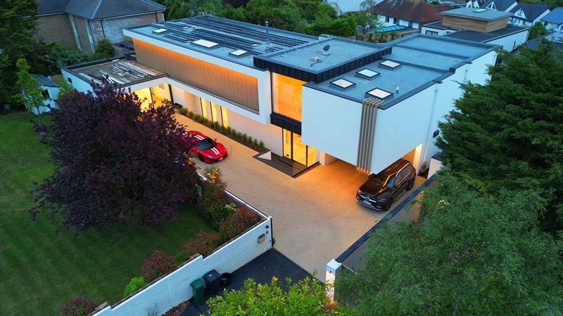 An aerial view of a contemporary eco home at dusk, its interior lit and cars on the drive