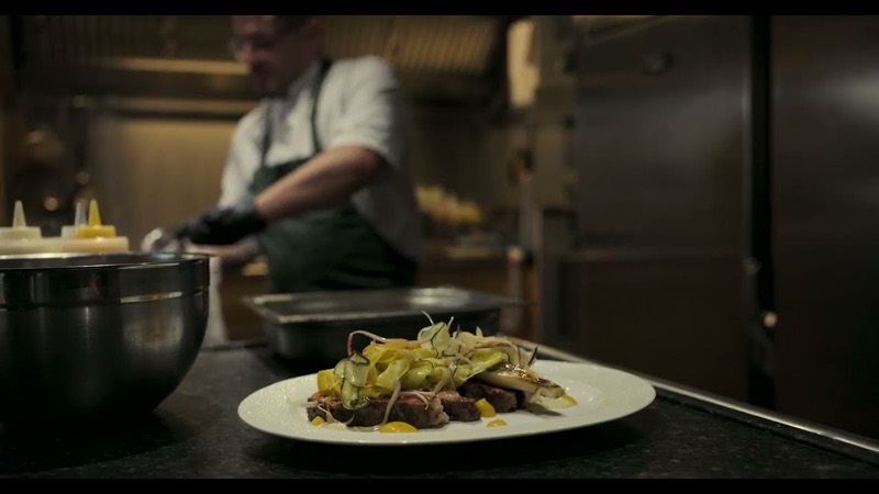 A plated dish on the pass, with a chef working behind it