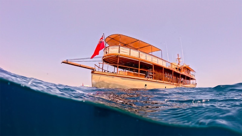 A classic wooden motor yacht at anchor, seen from the waterline at dusk