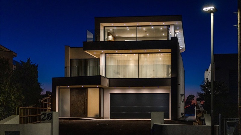 A contemporary three storey house lit from within at dusk