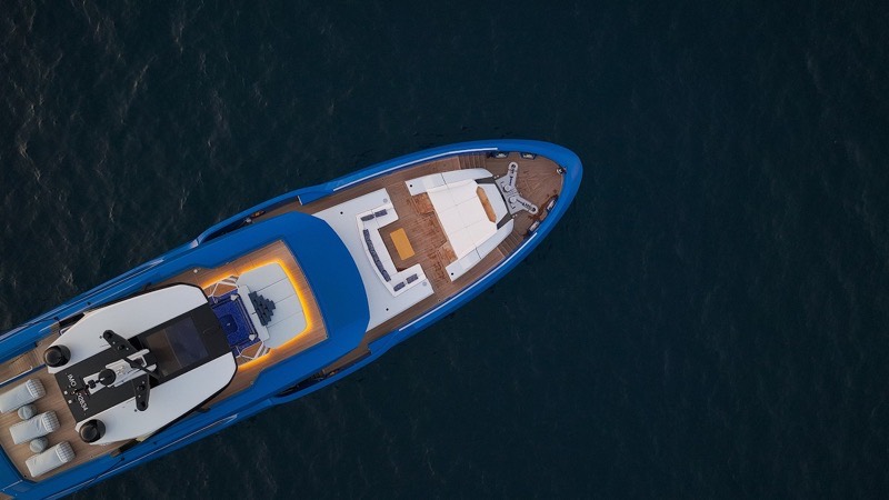 A blue hulled motor yacht seen from directly overhead at dusk, her foredeck lit and a tender stowed forward